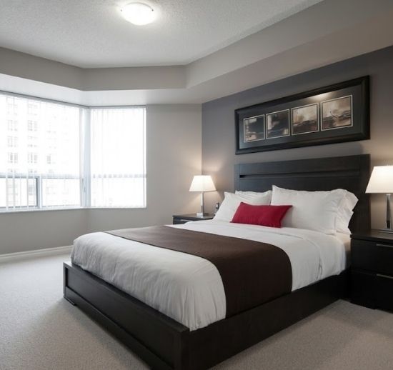 Modern bedroom with dark furniture, grey walls, and a red accent pillow.