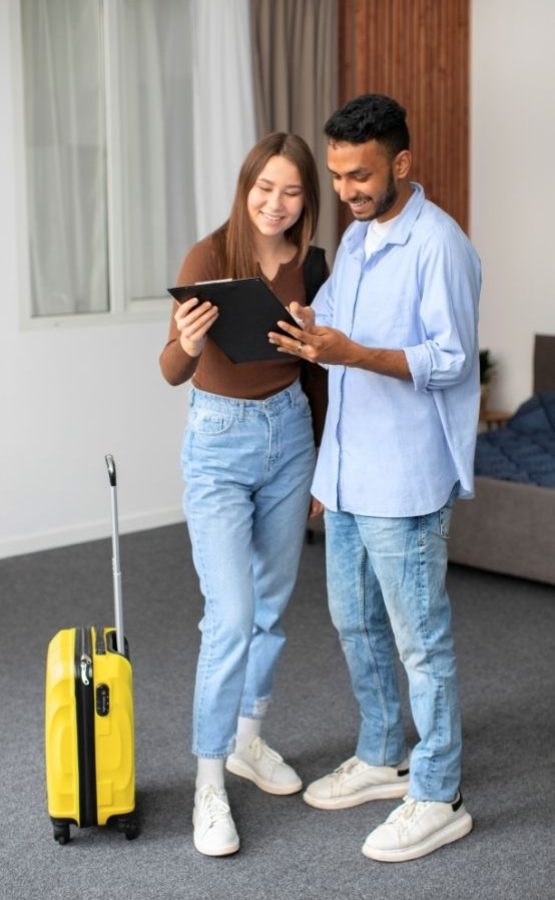 Host and guest reviewing a checklist for short let management in England, featuring a yellow suitcase.